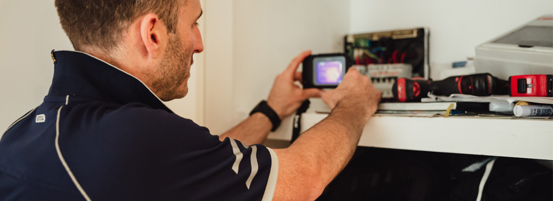 i-ELEC electrician using a thermal imaging camera to inspect an open residential switchboard during electrical fault finding and repairs in a Sydney home.