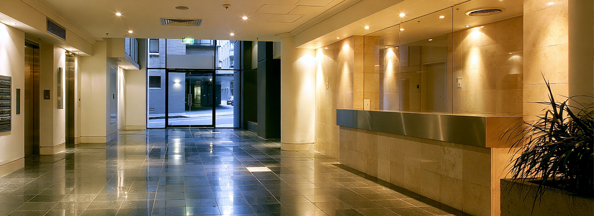 Wide panoramic architectural photograph of a modern Sydney apartment building lobby and common corridor, warm natural lighting, clean contemporary finishes, well-lit and carefully maintained, subtle Australian urban architecture